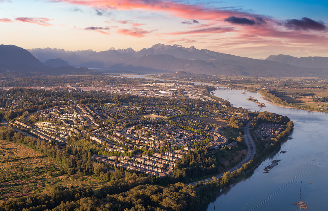 an arial image of a community beside a river with mountains in the distance