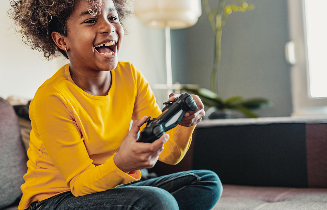 two boys sitting on a couch and laughing with headphones on and game controllers in their hands